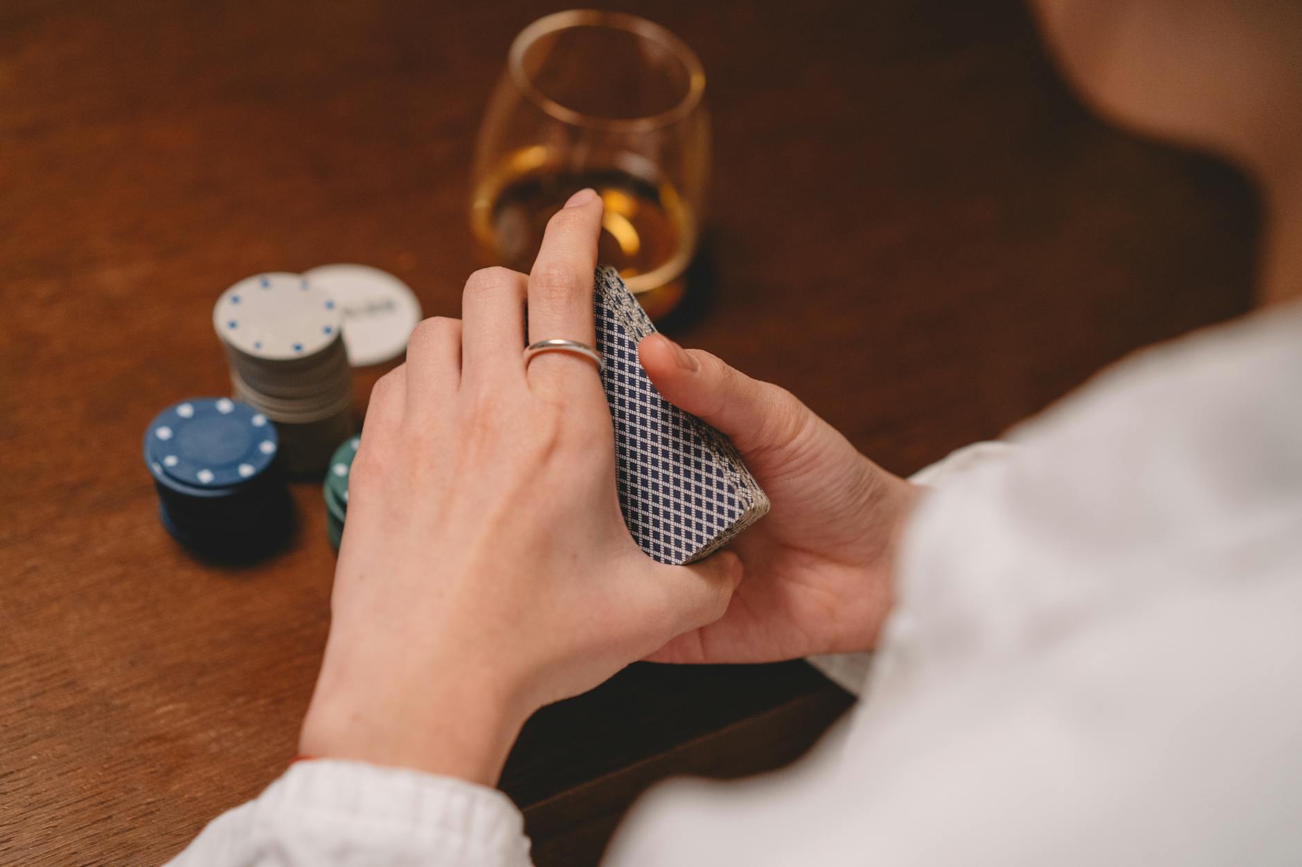 Close-up of a person's hands holding playing cards, with poker chips on a wooden table.