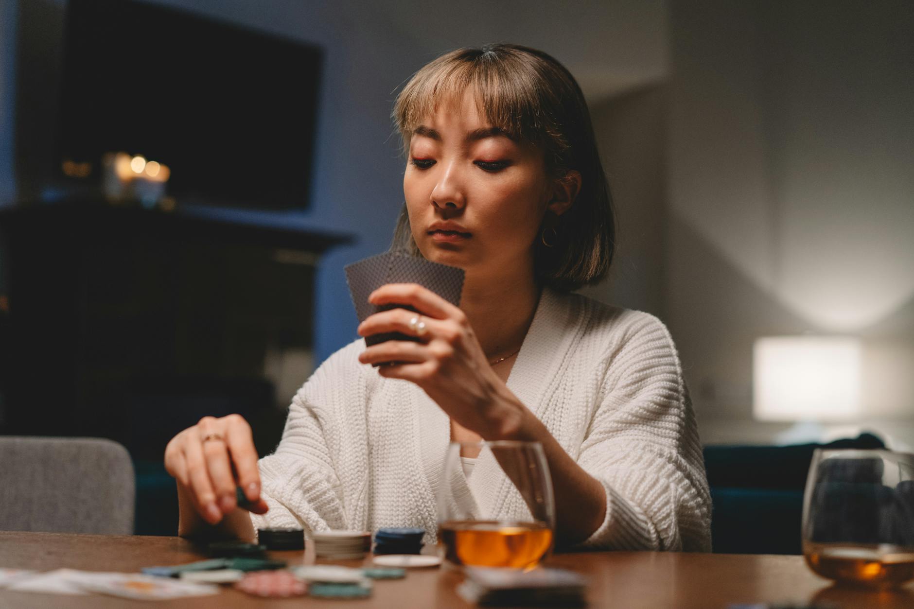 A woman in a cozy setting, seriously engaged in playing poker with cards and chips on the table.