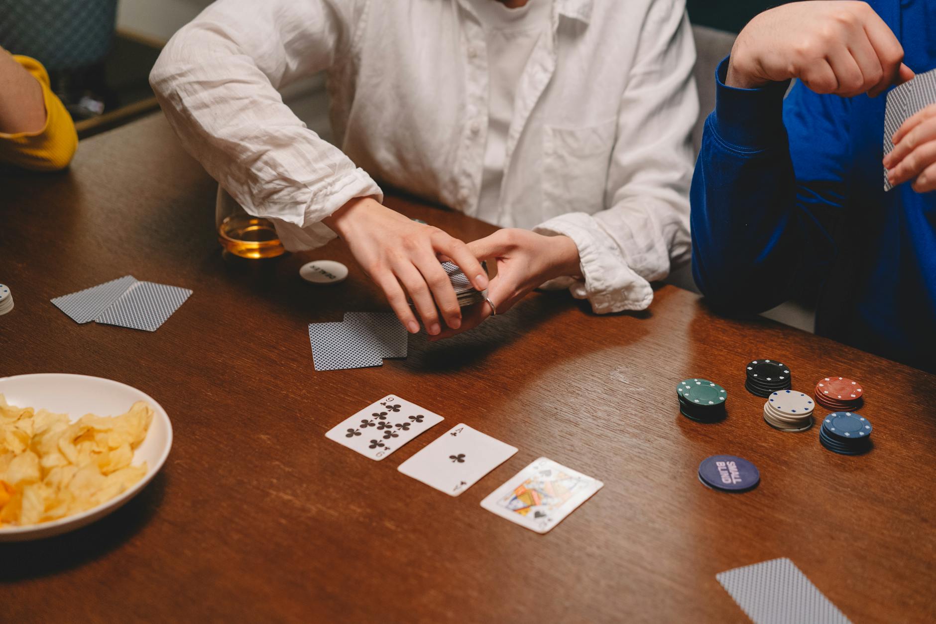 A group of people engaging in a casual poker game with chips and cards on a wooden table.