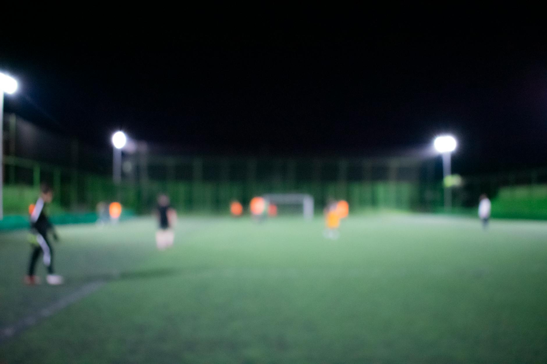Blurred image of a nighttime football match under bright stadium lights with players on the field.