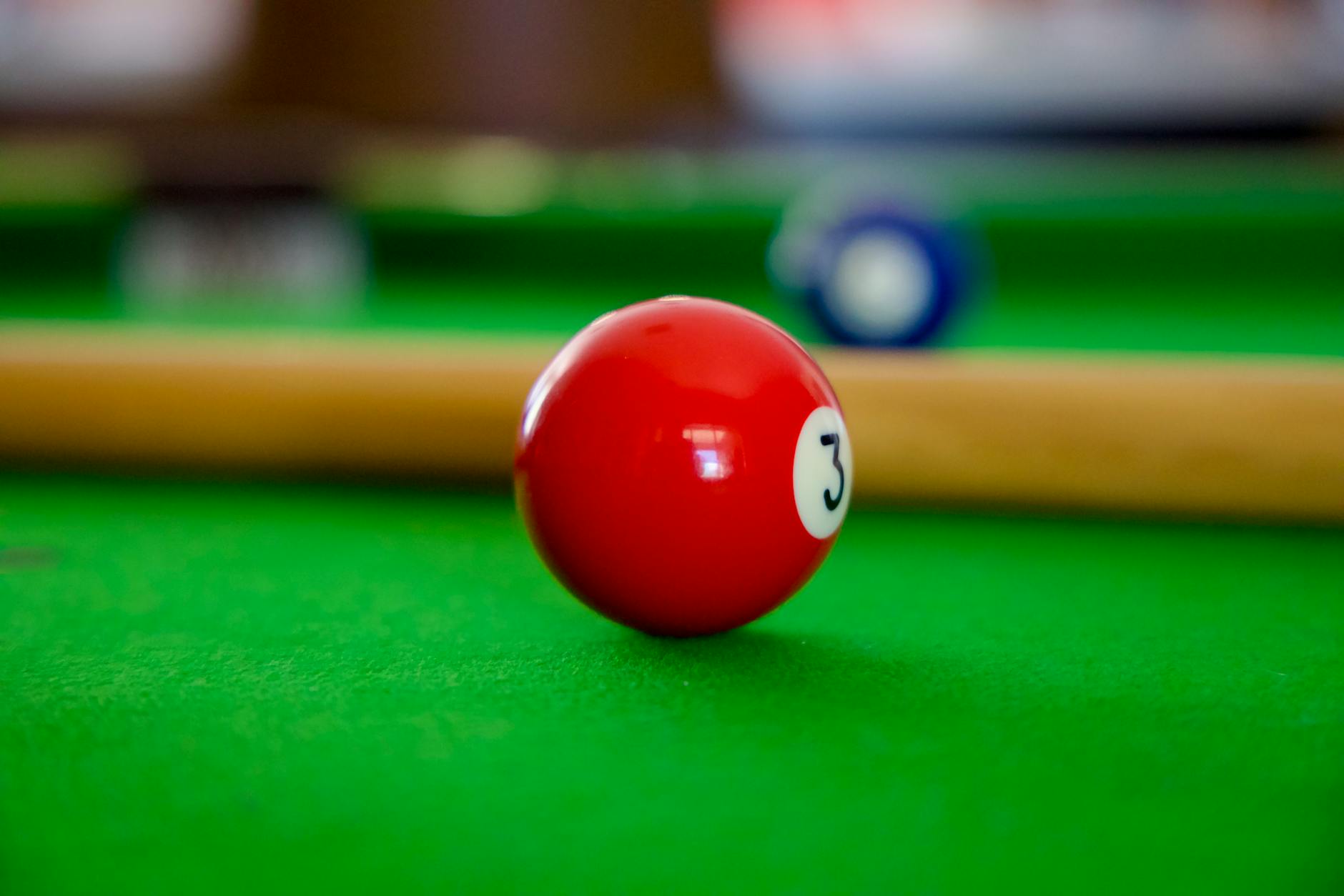 Detailed shot of red number 3 billiard ball on a vibrant green pool table surface.